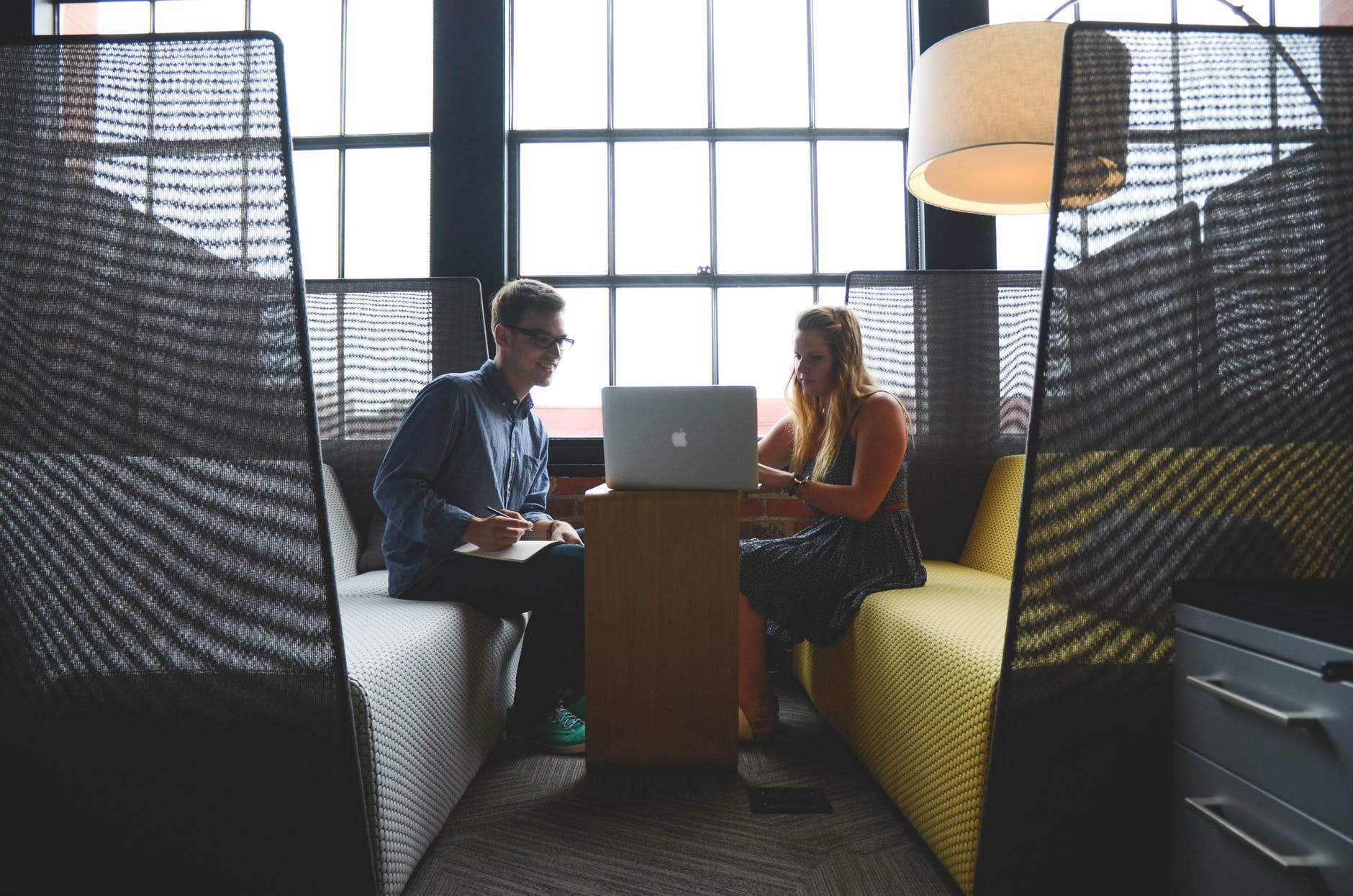 smiling man and woman both sitting on sofa both looking at silver macbook